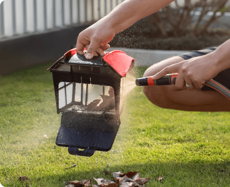 El usuario enjuaga sin esfuerzo las hojas de la gran cesta para residuos del iGarden Pool Cleaner K Pro con una manguera de jardín